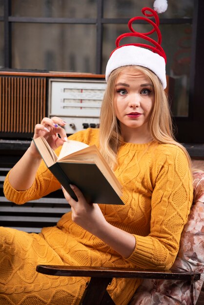 Junge Frau in Sankt-Hut, die mit geöffnetem Buch sitzt.