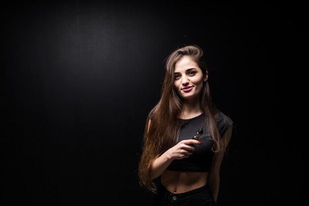 Junge Frau in Schwarz raucht eine elektronische Zigarette an der dunklen Wand