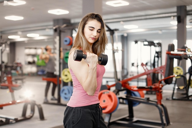 Junge Frau in Sportbekleidung, die im Fitnessstudio Übungen mit Hanteln macht