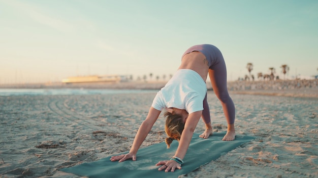 Junge Frau in Sportkleidung, die Yoga-Übungen am Strand macht Hübsches Mädchen, das Dehnübungen macht