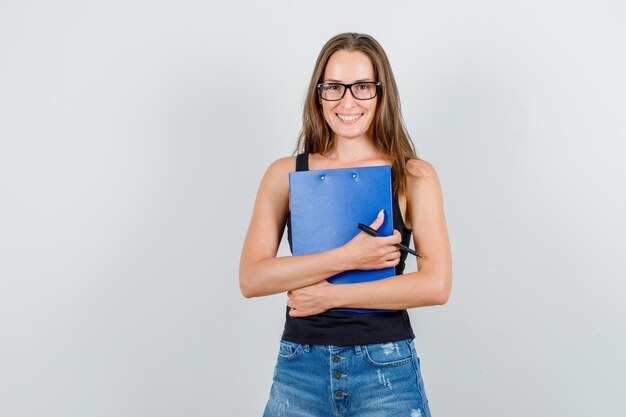 Junge Frau in Unterhemd, Shorts, Brille, die Klemmbrett und Stift hält und fröhlich schaut