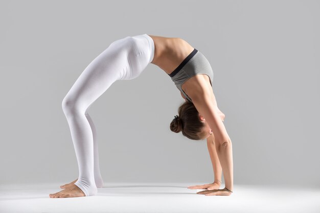 Junge Frau in Urdhva Dhanurasana Pose, grau Studio Hintergrund