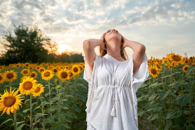 Junge Frau in weißem Kleid, die auf einem Feld mit Sonnenblumen steht