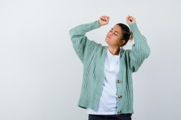 Junge Frau in weißem T-Shirt und mintgrüner Strickjacke, die Siegergeste zeigt und glücklich aussieht