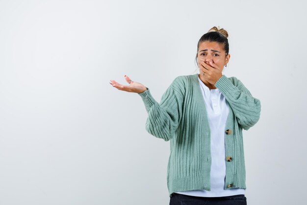 Junge Frau in weißem T-Shirt und mintgrüner Strickjacke, die wegen schlechten Geruchs die Nase kneift und genervt aussieht