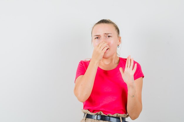 Junge Frau kneift die Nase wegen des schlechten Geruchs im T-Shirt und sieht angewidert aus