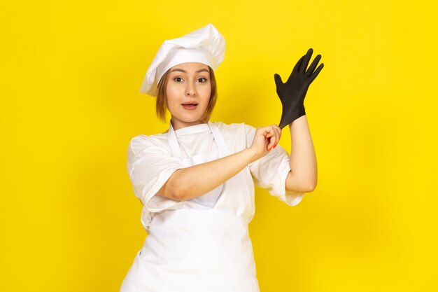 junge Frau kocht im weißen Kochanzug und in der weißen Kappe, die schwarzen Handschuh tragen