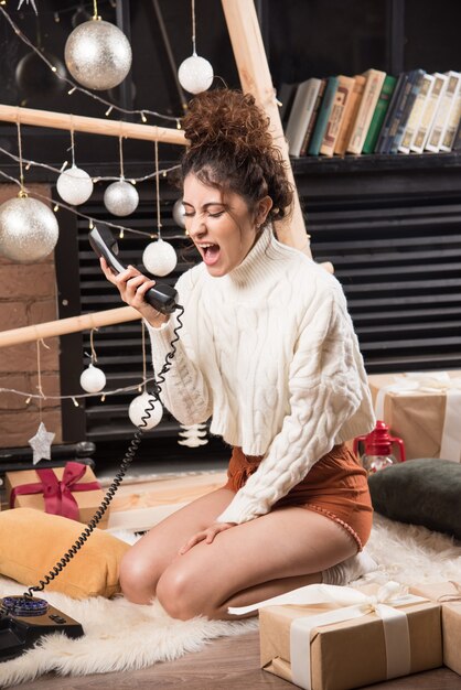 Junge Frau liegt auf einem flauschigen Teppich und schreit am Telefon