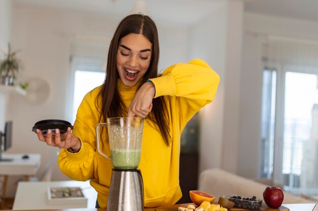 Junge Frau macht Smoothie mit Früchten Wunderschönes Mädchen, das in der Küche steht und Smoothie mit Obst und Gemüse zubereitet