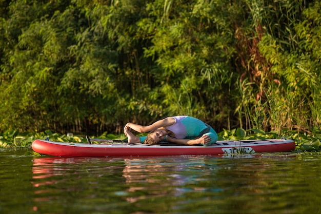 Junge Frau macht Yoga auf einem Stand Up Paddle Board SUP auf einem wunderschönen See oder Fluss. Das Konzept eines gesunden Lebensstils. Sport. Yoga. Hobby