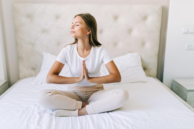 Junge Frau macht Yoga-Übungen auf dem Bett zu Hause