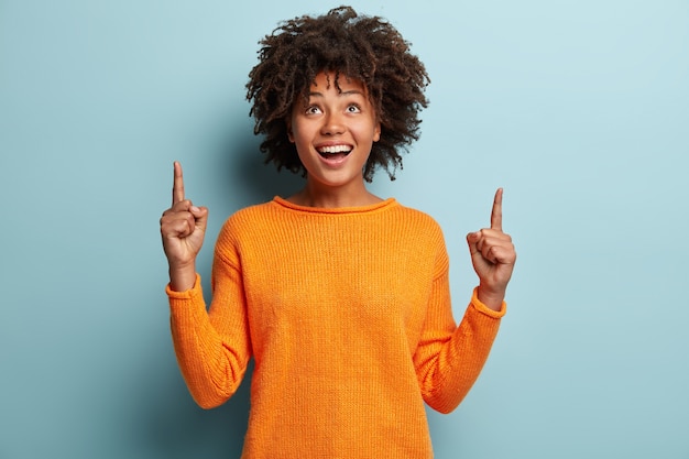 Junge Frau mit Afro-Haarschnitt, der orange Pullover trägt