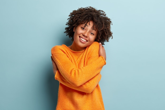 Junge Frau mit Afro-Haarschnitt, der orange Pullover trägt