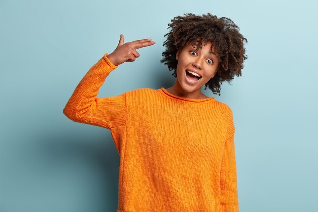 Junge Frau mit Afro-Haarschnitt, der orange Pullover trägt