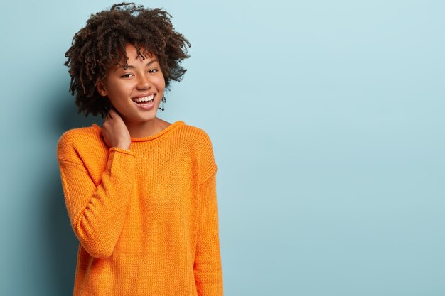 Junge Frau mit Afro-Haarschnitt, der orangefarbenen Pullover trägt