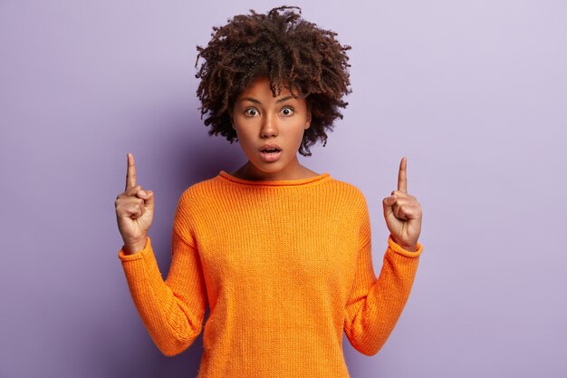 Junge Frau mit Afro-Haarschnitt, der orangefarbenen Pullover trägt