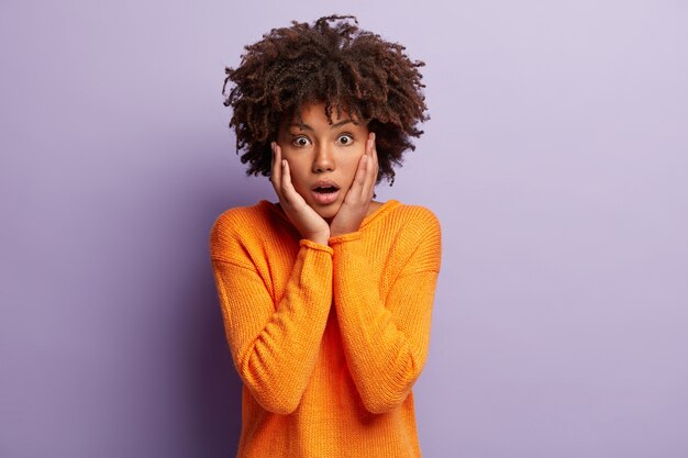 Junge Frau mit Afro-Haarschnitt, der orangefarbenen Pullover trägt