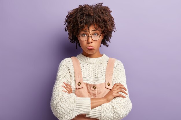 Junge Frau mit Afro-Haarschnitt, der Overalls und Pullover trägt