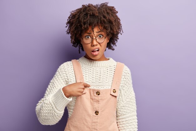 Junge Frau mit Afro-Haarschnitt, der rosa Overall und Pullover trägt