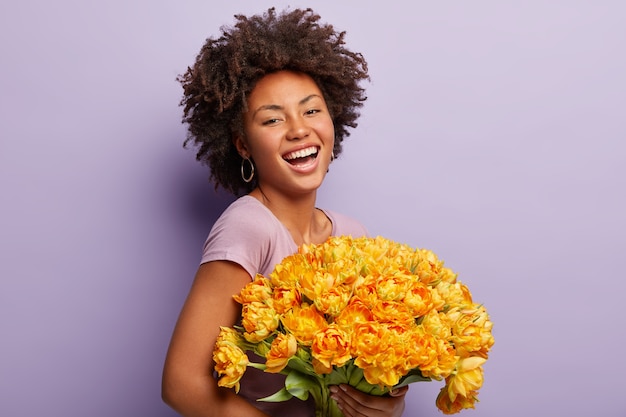 Junge Frau mit Afro-Haarschnitt, der Strauß der gelben Blumen hält