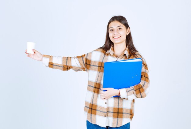 Junge Frau mit blauem Ordner und Tasse Kaffee auf weißer Wand.