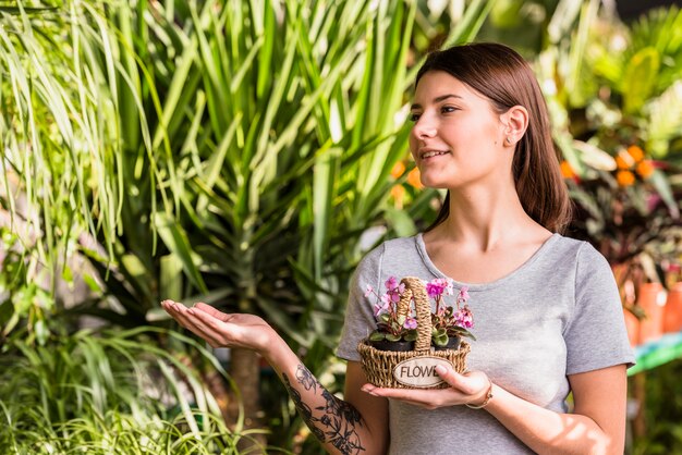 Junge Frau mit Blumen im Korb, der an den Grünpflanzen darstellt