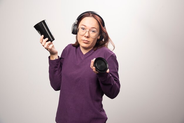 Junge Frau mit Brille, die in den Kopfhörern auf einem weißen Hintergrund aufwirft. Hochwertiges Foto