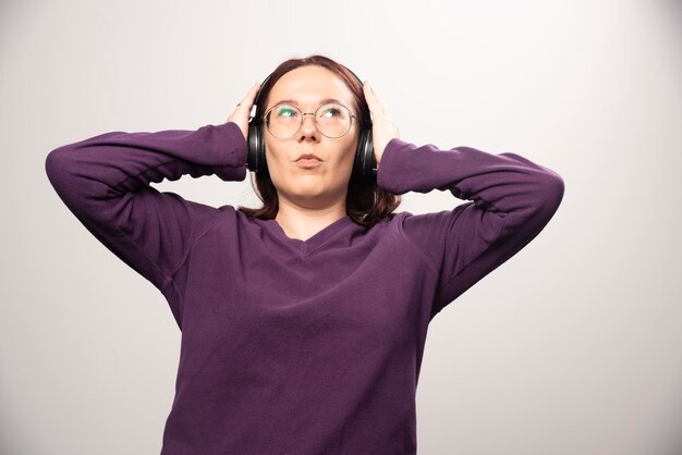 Junge Frau mit Brille, die Musik über Kopfhörer auf einem Weiß hört. Foto in hoher Qualität