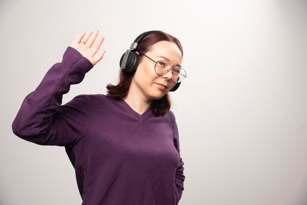 Junge Frau mit Brille, die Musik über Kopfhörer auf einem Weiß hört. Foto in hoher Qualität