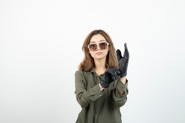 Junge Frau mit Brille, die schwarze Handschuhe über Weiß anprobiert. Foto in hoher Qualität