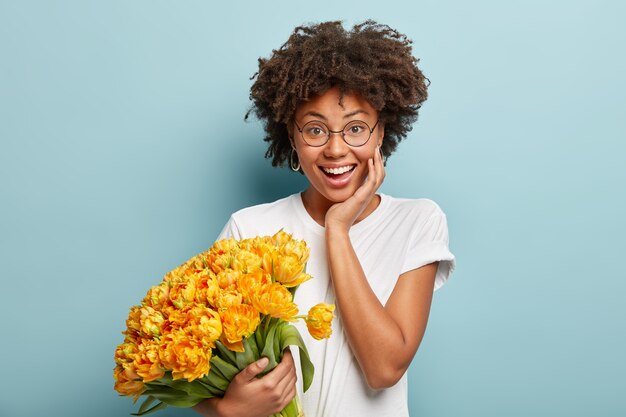 Junge Frau mit dem gelockten Haar, das Strauß der gelben Blumen hält