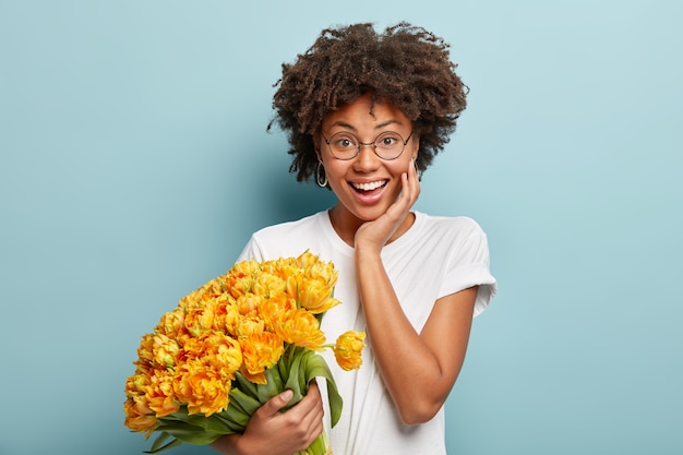 Junge Frau mit dem gelockten Haar, das Strauß der gelben Blumen hält