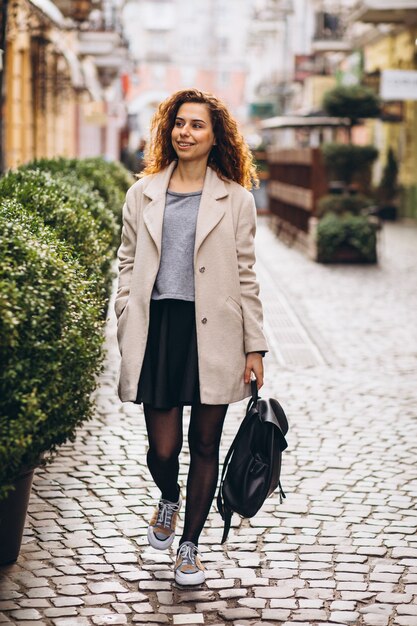 Junge Frau mit dem gelockten Haar gehend an einer Caféstraße