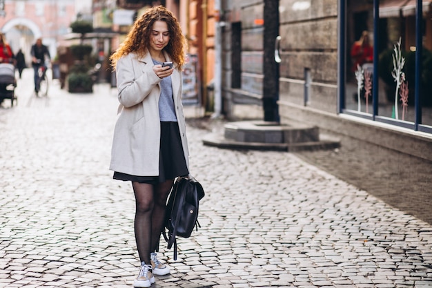 Kostenloses Foto junge frau mit dem gelockten haar unter verwendung des telefons an der straße