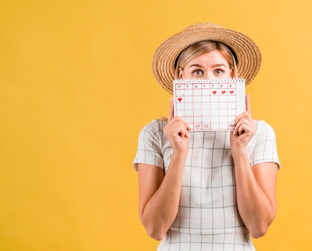 Junge Frau mit dem Hut, der ihr Gesicht mit Menstruationskalender bedeckt