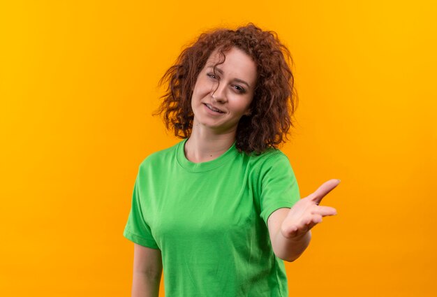 Junge Frau mit dem kurzen lockigen Haar im grünen T-Shirt, das beruhigende Geste mit Handstand macht