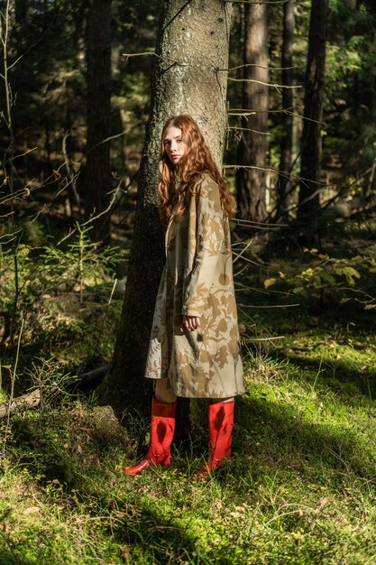Junge Frau mit dem langen roten Haar in einem Leinenkleid Pilze im Wald erfassend