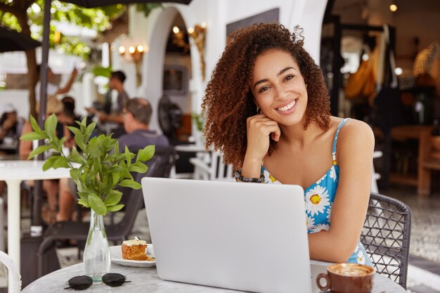 Junge Frau mit dem lockigen Haar, das im Café mit Laptop sitzt