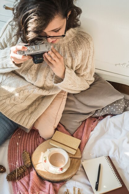 Junge Frau mit der Fotokamera, die auf Decke mit Kissen sitzt