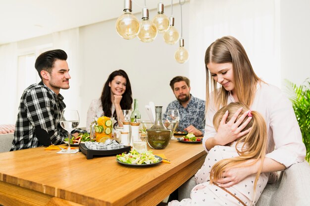 Junge Frau mit der kleinen Tochter und Freunde, die am Tisch sitzen