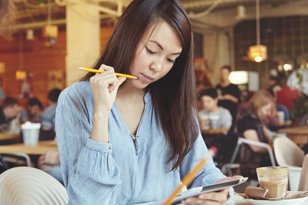 Junge Frau mit dunklem Haar unter Verwendung der Tablette im Café