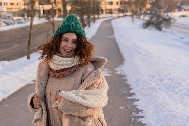 Junge Frau mit dunklem lockigem Haar in einer Wintermütze, warm gekleidet, Winterfrost, sonniger Tag draußen.