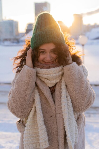 Junge Frau mit dunklem lockigem Haar in einer Wintermütze, warm gekleidet, Winterfrost, sonniger Tag draußen.