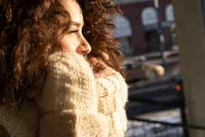 Kostenloses Foto junge frau mit dunklem, lockigem haar, nahaufnahme, warm gekleideter schal, winterfrost, sonniger tag auf der straße in der stadt.