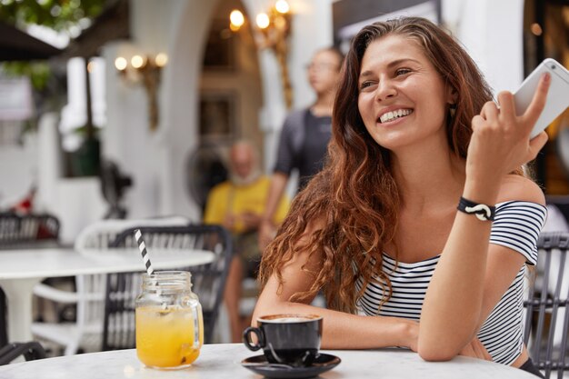 junge Frau mit dunklen langen Haaren, die am Telefon in einem Café sprechen