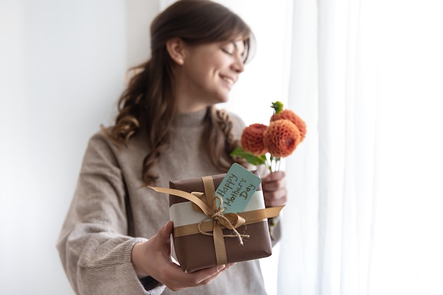 Junge Frau mit einem Geschenk zum Muttertag und einem Blumenstrauß in den Händen