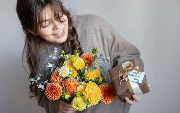 Junge Frau mit einem Geschenk zum Muttertag und einem Blumenstrauß in den Händen