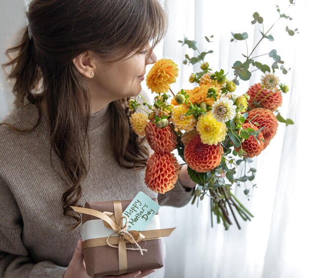 Junge Frau mit einem Geschenk zum Muttertag und einem Blumenstrauß in ihren Händen