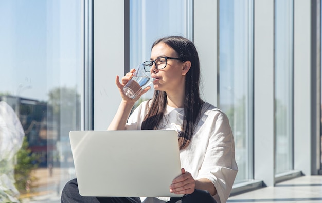 Junge Frau mit einem Glas Wasser vor einem Laptop am Morgen