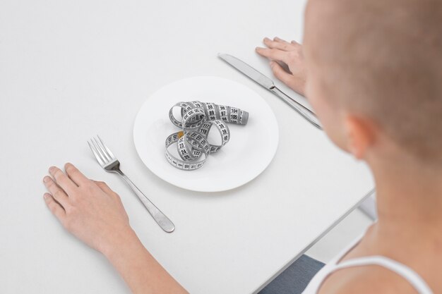 Junge Frau mit einer Essstörung mit einem Maßband auf dem Teller
